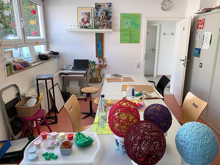 Eine Tischreihe mit Bildern und Bastelprojekten darauf. Zu erkennen sind zum Beispiel Ballons, die mit Schnüren beklebt sind oder auch eine bemalte Gipshand (Caritasverband Darmstadt e. V. / Jens Berger)