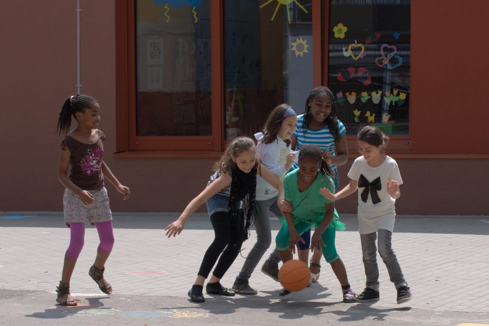 Kinder spielen auf einem Schulhof Basketball. 