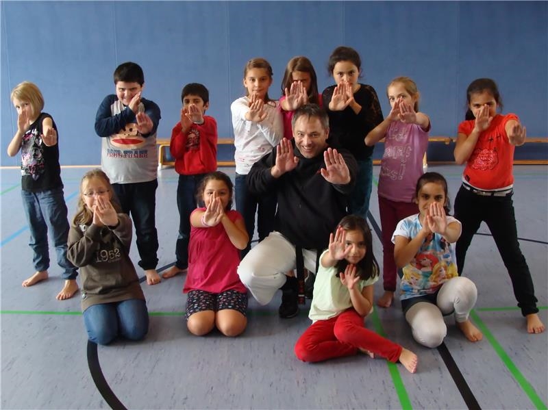 12 Jungen und Mädchen zusammen mit ihrem Karate-Trainer posieren für ein Gruppenfoto und zeigen einen "Handgriff" 