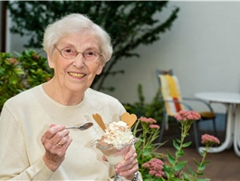 Eine Seniorin sitzt im schattigen Innenhof des Seniorenzentrums und isst ein Eis. / Werner Krüper