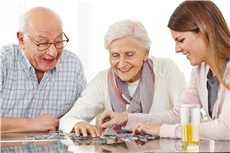 Ein älterer Mann und eine ältere Frau sitzen mit einer jungen Mitarbeiterin eines Altenzentrums beim Puzzlen zusammen.  / Fotolia