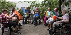 Im Innenhof vom Caritas-Altenzentrum Heilig Geist sitzen Seniorinnen und Senioren in einer Runde zusammen und beschäftigen sich unter Anleitung einer Mitarbeiterin mit bunten Tüchern.  / Carinet