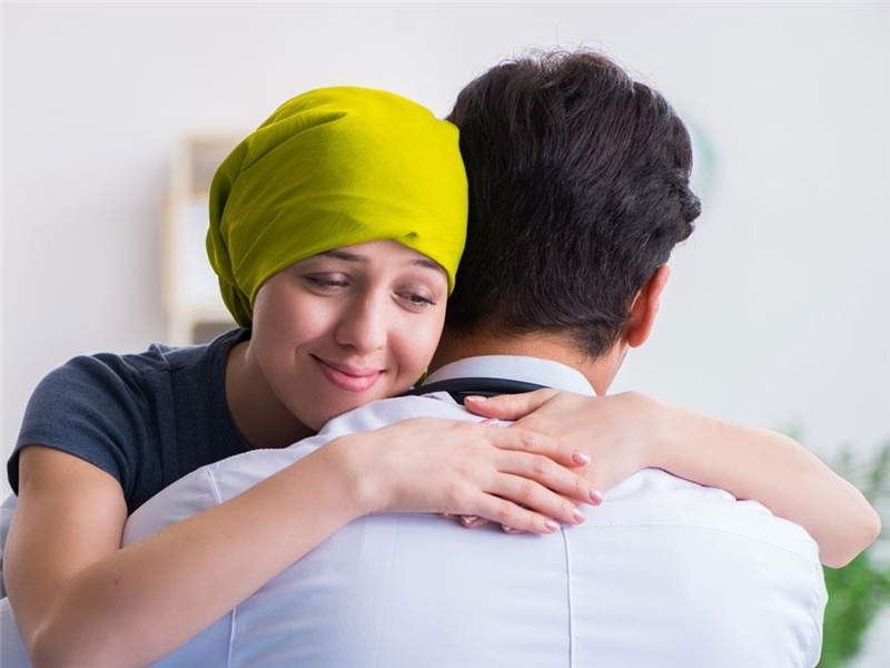 Krebskranke junge Frau mit Kopftuch in den Armen ihres Freundes