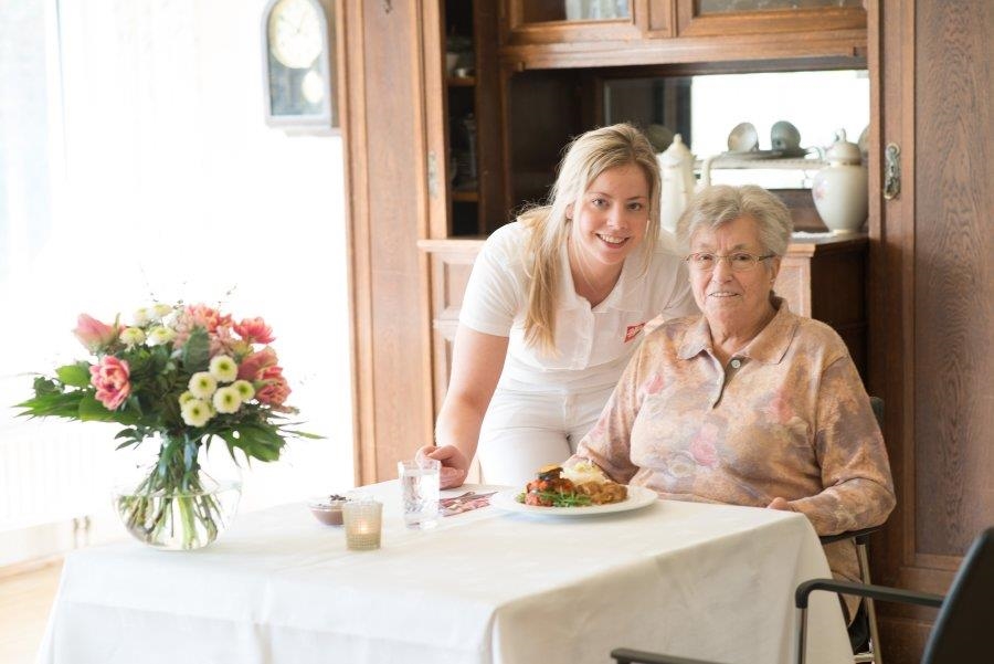 Eine junge weibliche Pflegekraft serviert einer Seniorin das Mittagsessen (Udo Keus)
