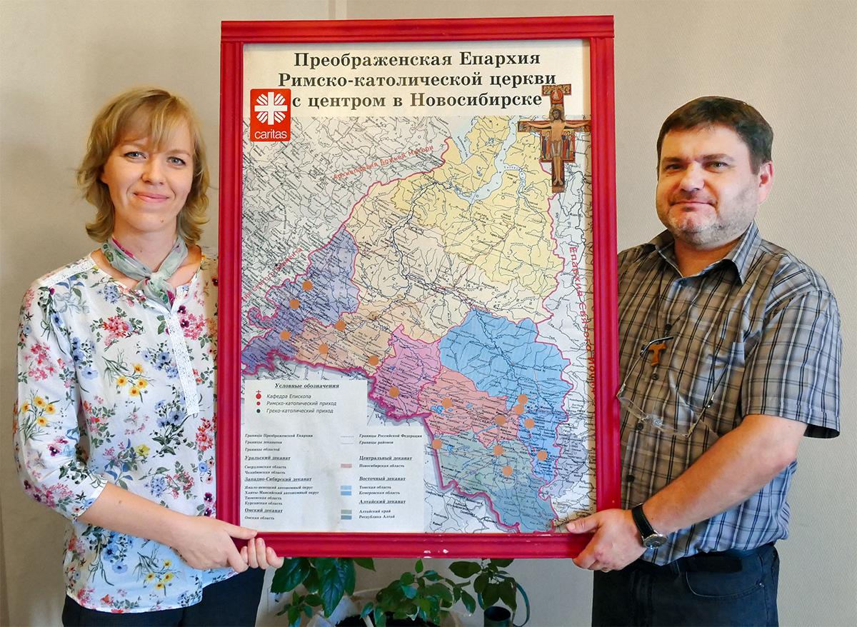Der Direktor des Diözesan-Caritasverbandes Novosibirsk und seine Stellvertreterin halten eine Karte der Diözese Novosibirsk hoch, die in einen roten Rahmen gefasst ist  (Christian Heidrich)