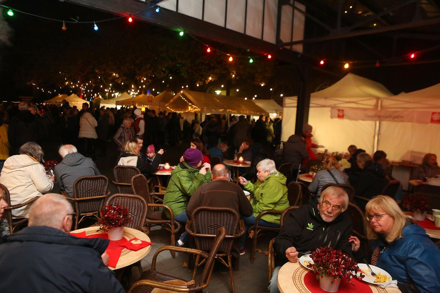 Besucher sitzen auf Stühlen und an Café-Tischen unter dem Dach im Zentrum Altenberg und essen/trinken. 