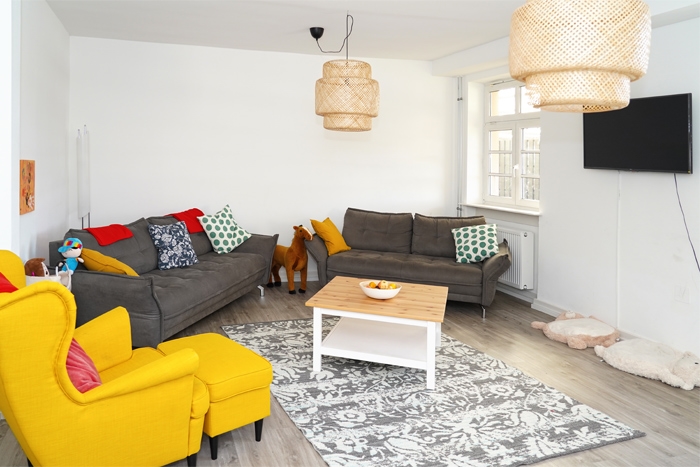 Wohnzimmer mit Sessel und Sofas, Tisch, Korblampen einem Fernseher und einem Stoffpferd (Caritasverband Darmstadt e. V. / Jens Berger)