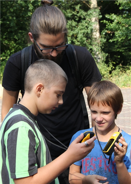 Zwei Kinder und ein Erwachsener beschäftigen sich mit einem GPS-Gerät. 