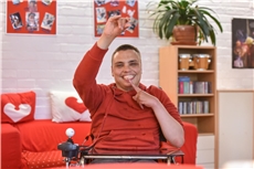 Junger Mann mit Behinderung hebt seinen Arm und lacht breit in die Kamera / Deutscher Caritasverband / Harald Oppitz, KNA