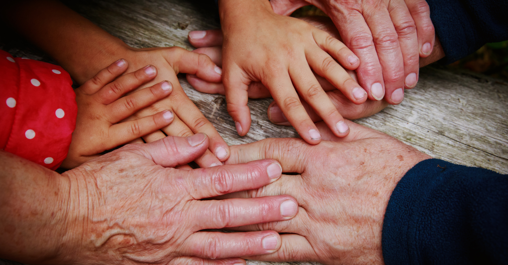 Faltige Hände von älteren Menschen und kleine Hände von Kindern liegen übereinander und nah beieinander. (Symbolfoto)