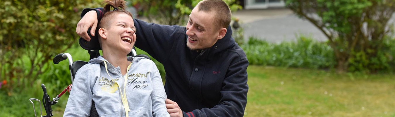 Betreuer legt seinen Arm um junge Frau mit Behinderung, die lacht