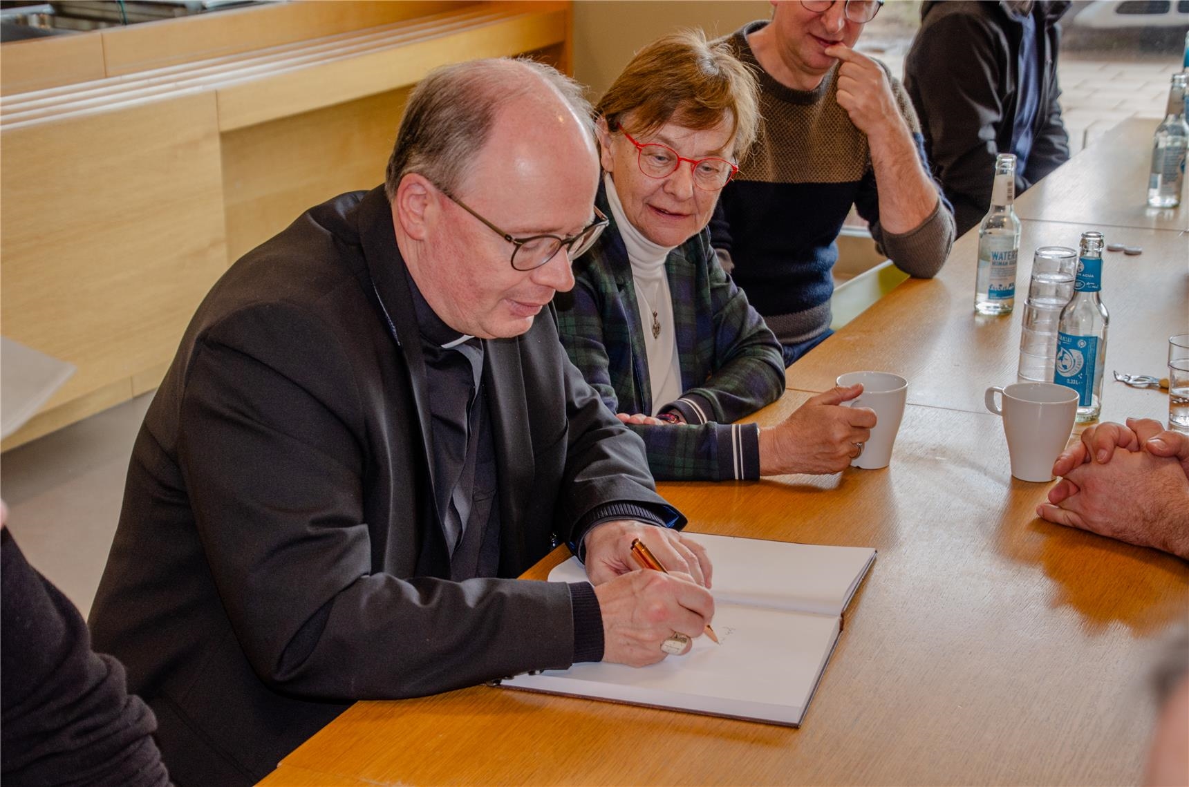 Ein Mann schreibt in ein Gästebuch, während eine Frau ihm dabei zusieht. (Caritasverband für Saarbrücken und Umgebung e.V. (Götz Plettke)