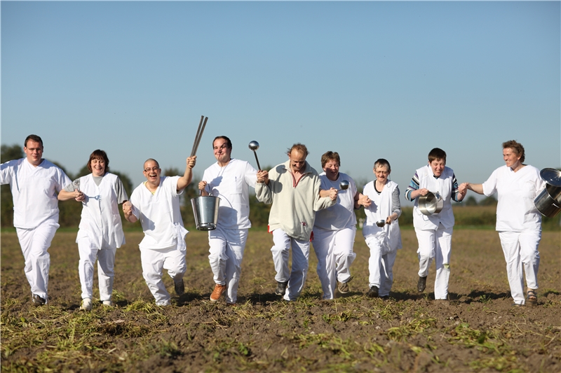 KüchenmitarbeiterInnen rennen über ein Feld und schwingen Kochlöffel und Rührbesen (©caritasverband bocholt)
