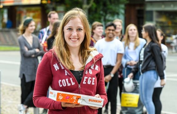 Junge Frau mit Donut-Schachtel in der Hand lächelt in die Kamera (Deutscher Caritasverband/Harald Oppitz, KNA)