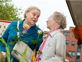 Zwei Seniorinnen stehen an einem Marktstand und riechen an einer Blume / Werner Krüper