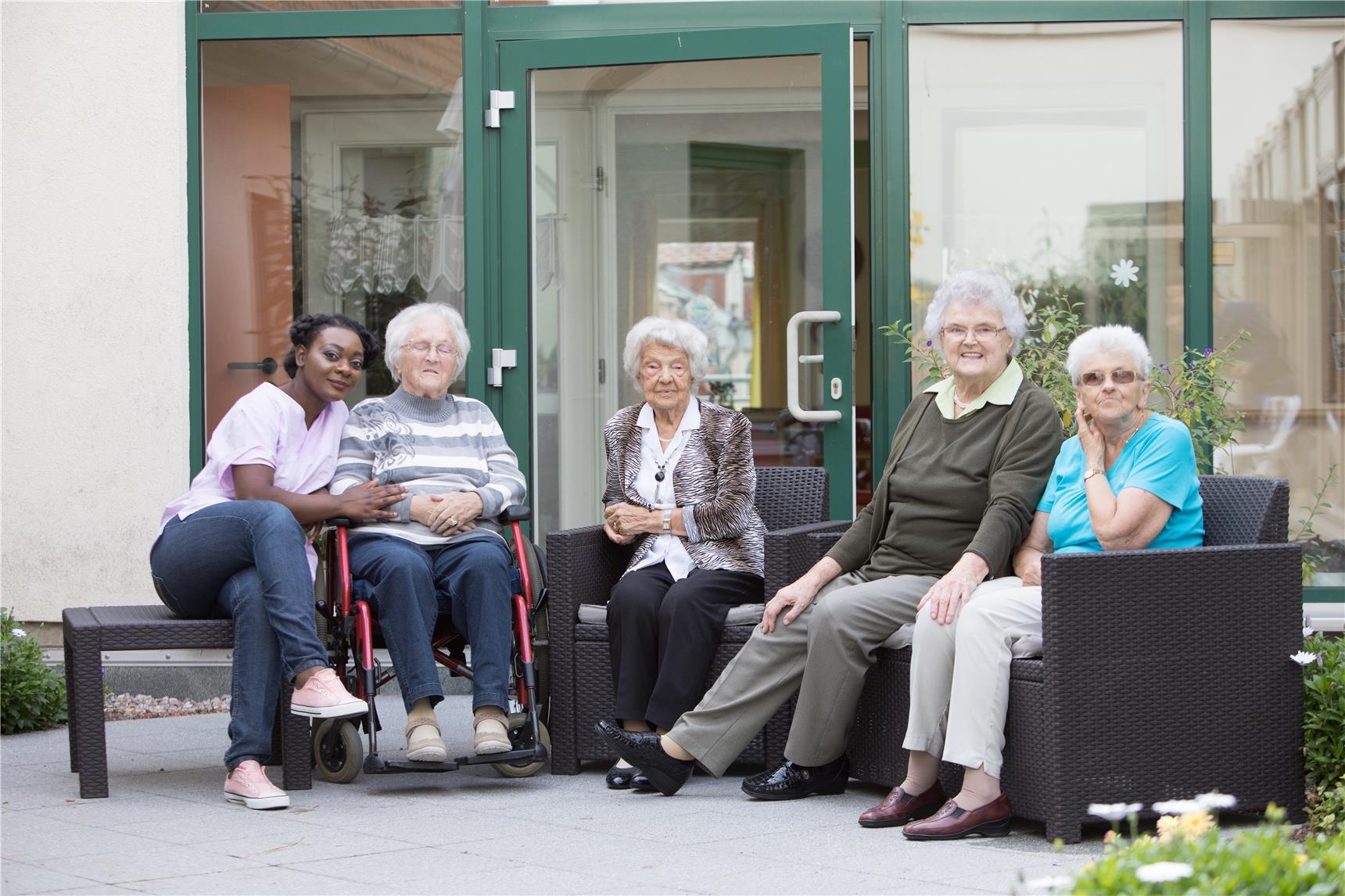 Bewohnerinnen und Pflegekraft in Sitzgruppe im Außenbereich 