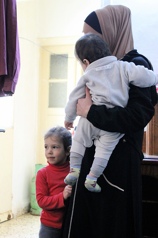 Eine Frau steht mit zwei Kindern in einem Raum. Das eine Kind hält sie auf dem Arm, das zweite Kind steht dicht neben ihr. (Markus Harmann)