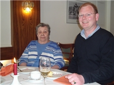 Ein Angehöriger sitzt zusammen mit seiner alten Mutter am festlich gedeckten Tisch.