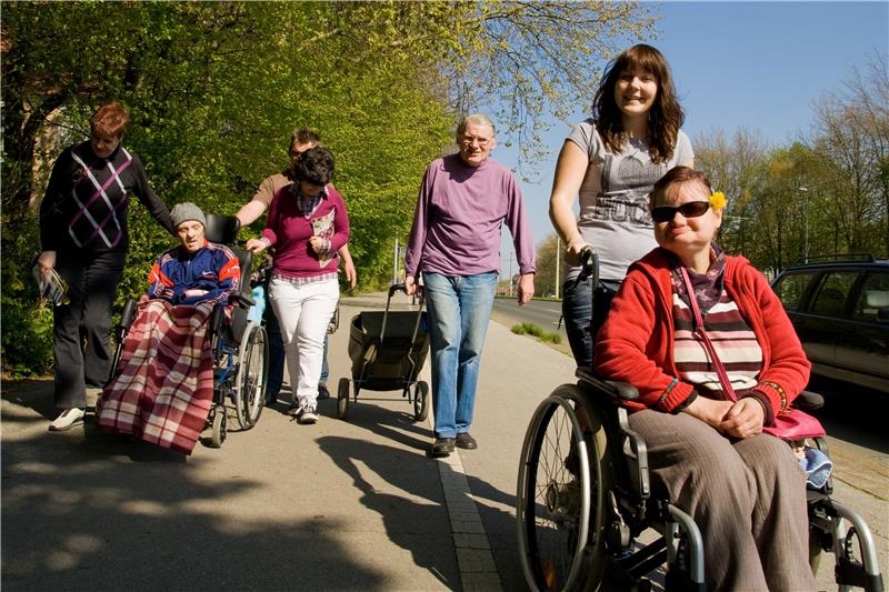 Betreuer und Bewohner in Rollstühlen unterwegs auf einem Bürgersteig 