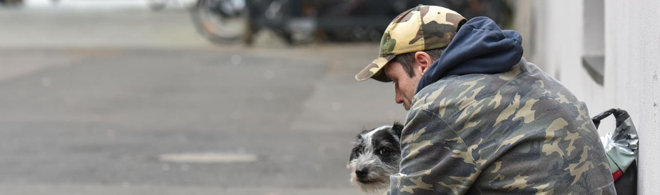 Wohnungsloser sitzt mit seinem Hund auf der Straße