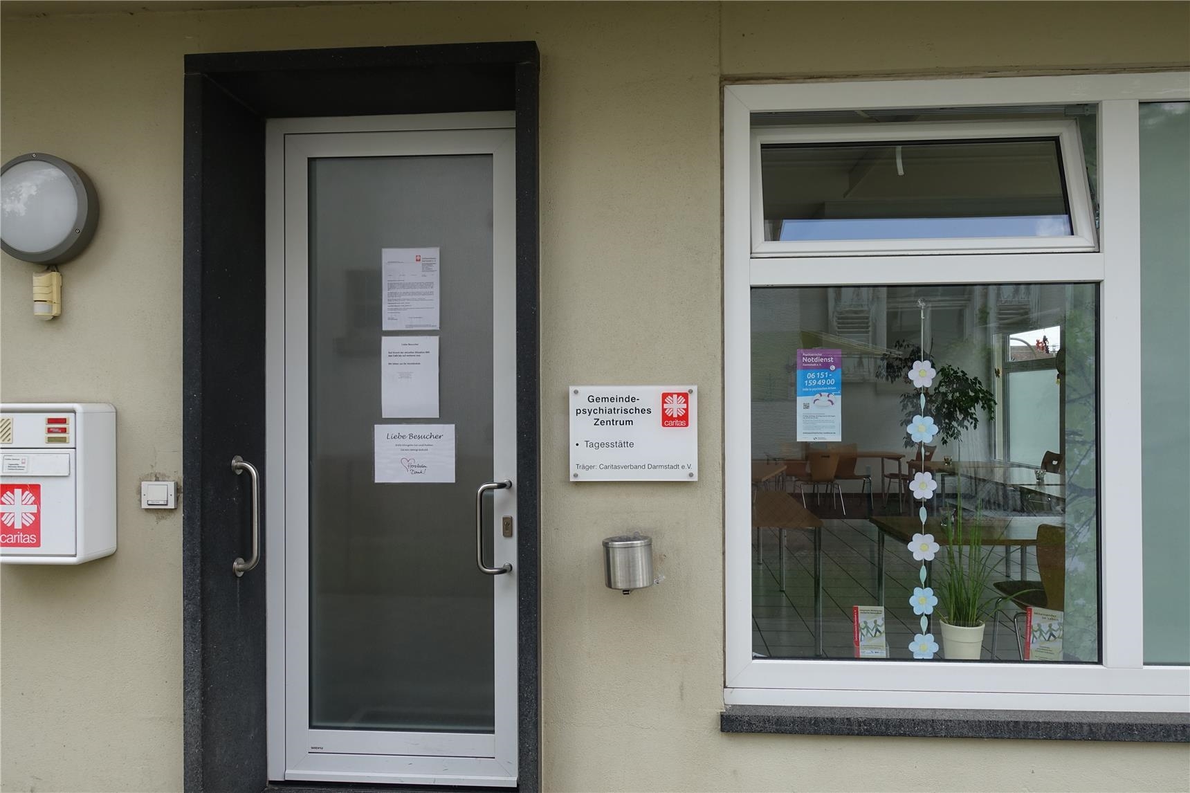 Gebäudefront mit Tür und Schild, auf welchem steht: Gemeindepsychiatrisches Zentrum Griesheim, Tagesstätte (Caritasverband Darmstadt e. V. / Jens Berger)