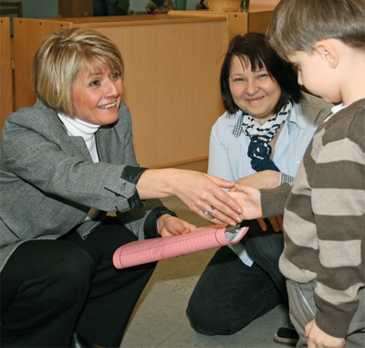 Staatssekretärin Zülfiye Kaykin kniet vor einem Jungen und schüttelt ihm die Hand. Zwischen den Beiden kniet eine Frau. 