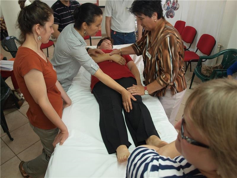 Vier Frauen stehen um ein Krankenbett, in dem eine weitere Frau liegt. Das Foto ist von schräg oben aufgenommen. (Caritas)