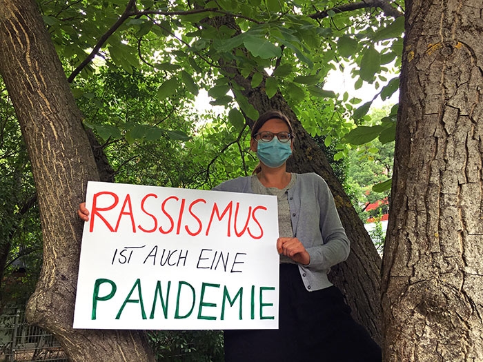 Frau mit Schild mit der Aufschrift Rassismus ist auch eine Pandemie (Caritasverband Darmstadt e. V.)