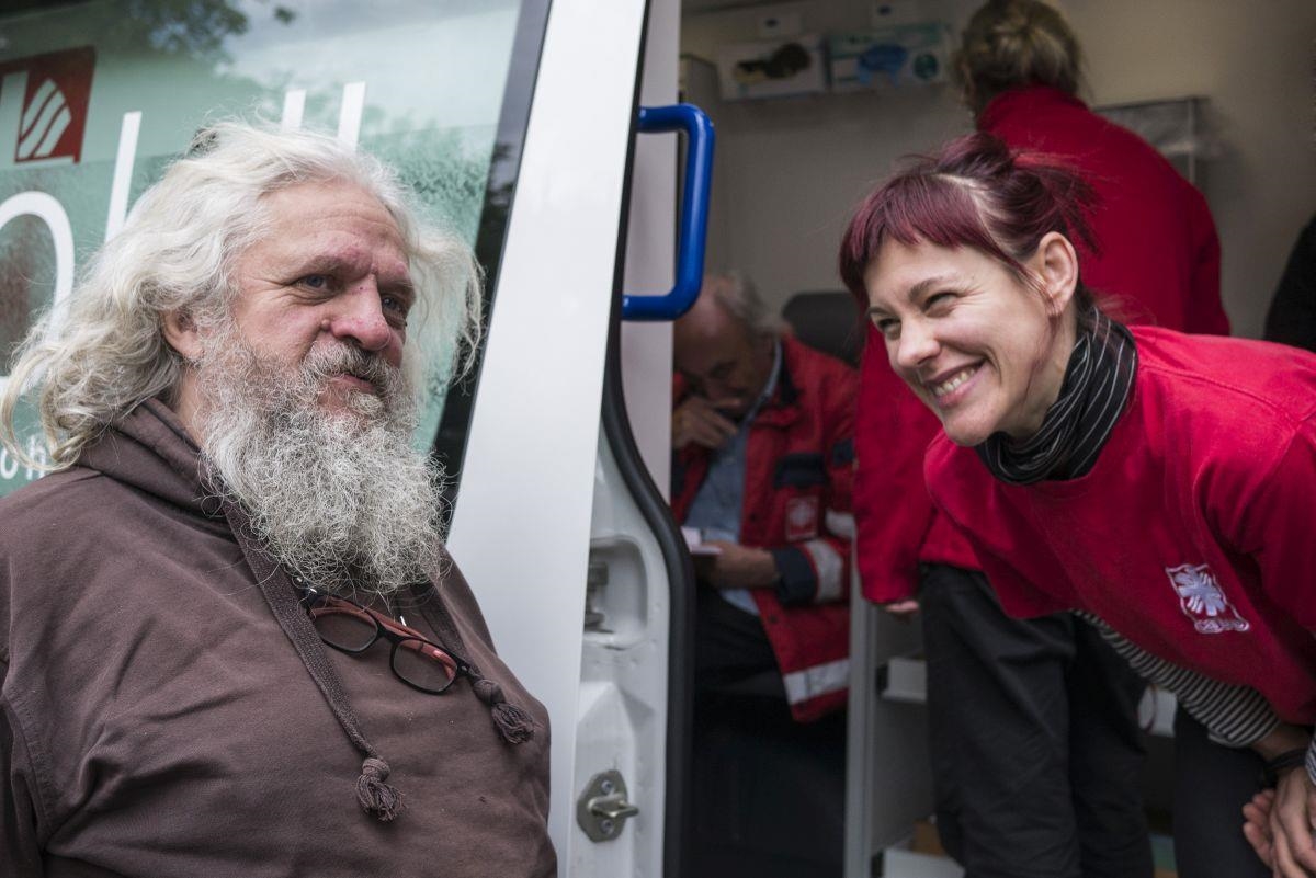 Älterer Obdachloser mit weißen haaren und Bart vor dem Arztmobil mit Sozialarbeiterin