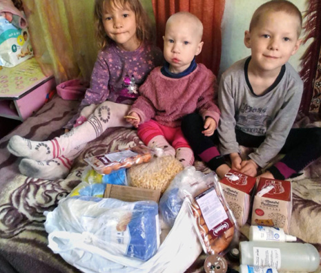 Drei Kinder in der ukrainischen Stadt Winnyzja, die vor einer ausgepackten Spendentüte der Caritas-Spes sitzen (Foto: Caritas-Spes)