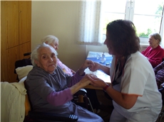 Eine Mitarbeiterin hält beide Hände einer älteren Dame, die im Caritas-Altenzentrum St. Anton wohnt. Die Bewohnerin blickt mit einem Lächeln zum Fotografen.  / Caritas-Altenzentrum St. Anton