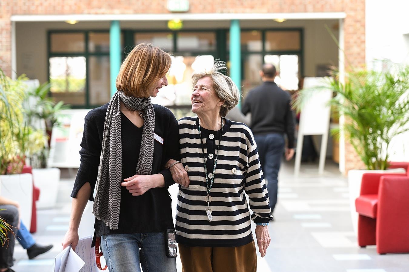 Eine Seniorin und ein junge Frau gehen untergehakt spazieren und unterhalten sich.