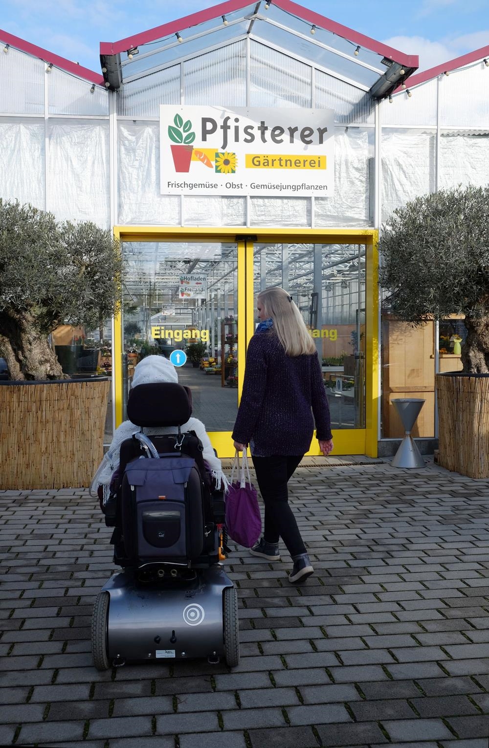 Zwei Frauen, eine davon im Rollstuhl laufen auf eine Gärtnerei zu. (Ulrike Seifart)