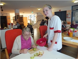 Eine alte Frau sitzt an einem Tisch mit einer Schüssel in der Hand. Eine junge Frau steht neben ihr. / Foto: Schedlbauer