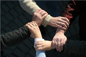 Vier Arme, die ineinandergreifen und ein Netzwerk der helfenden Hände symbolisieren.