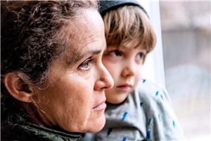 A woman looks discouraged out of a window with a little boy in her arms