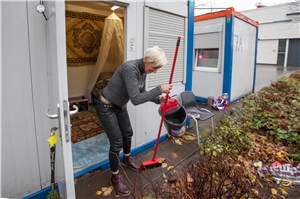 Frau putzt den Boden vor ihrem Wohncontainer