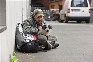 obdachloser Mann schaut mit seinem Hund dem Geschehen auf der Straße zu