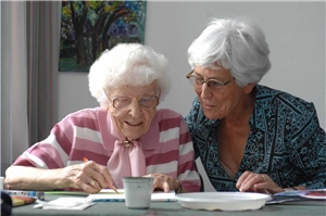 eine ältere Begleiterin unterstützt eine ältere Dame beim Ausfüllen von Formularen