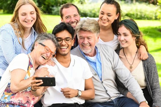 Junge und ältere Menschen lachen beim Blick auf ein Smartphone