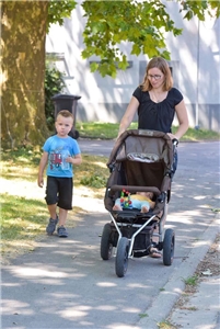 Mutter mit Baby im Kinderwagen läuft mit Kleinkind spazieren