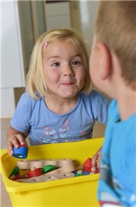 Kleines Mädchen mit Spielsachen schaut ihren Bruder frech an