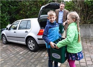 Tochter und Sohn helfen Vater beim Entladen von Getränkekisten aus dem Auto