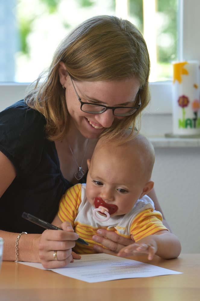Mutter mit Baby auf dem Schoß beim Schreiben