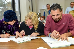 Helferin und zwei Flüchtlinge im Deutschkurs