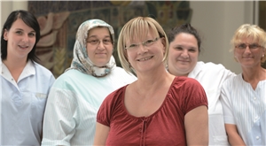 Eine Mitarbeiterin eines Pflegeteams blickt in die Kamera, im Hintergrund stehen ihre Kolleginnen