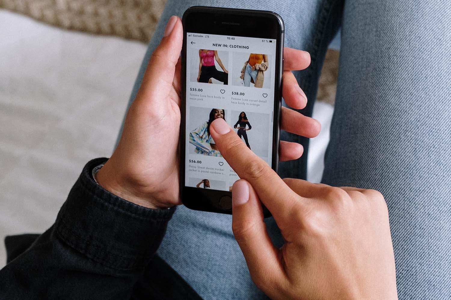 Zwei Hände halten ein Handy auf dessen Display ein Onlineshop für Mode zu sehen ist.