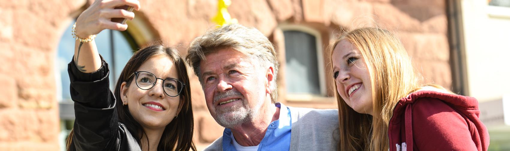 Zwei junge Frauen machen mit dem Handy ein Selfie mit einem älteren Mann