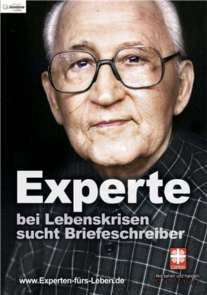 Älterer Mann schaut aufmerksam, auf dem Plakat steht "Experte für Lebenskrisen sucht Briefeschreiber