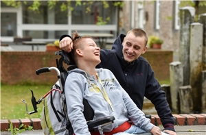 Lachende junge Frau im Rollstuhl mit Betreuer
